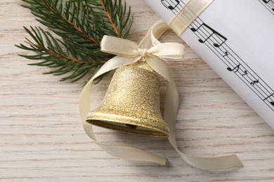 Golden shiny bell with bow, music sheet and fir twig on wooden table, flat lay. Christmas decoration