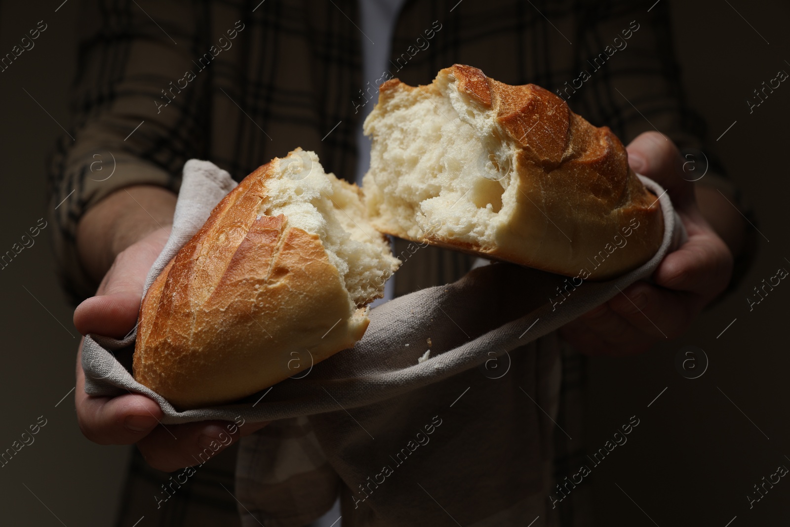 Photo of Man breaking loaf of fresh bread on dark background, closeup