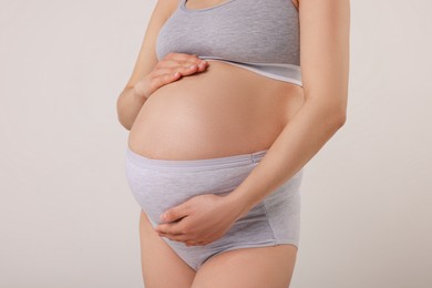 Photo of Pregnant woman in comfortable maternity underwear on grey background, closeup