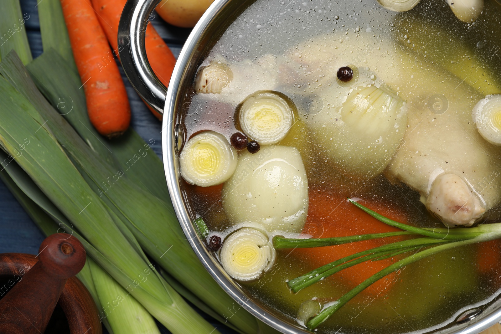 Photo of Pot with tasty bouillon and different ingredients on blue wooden table, flat lay