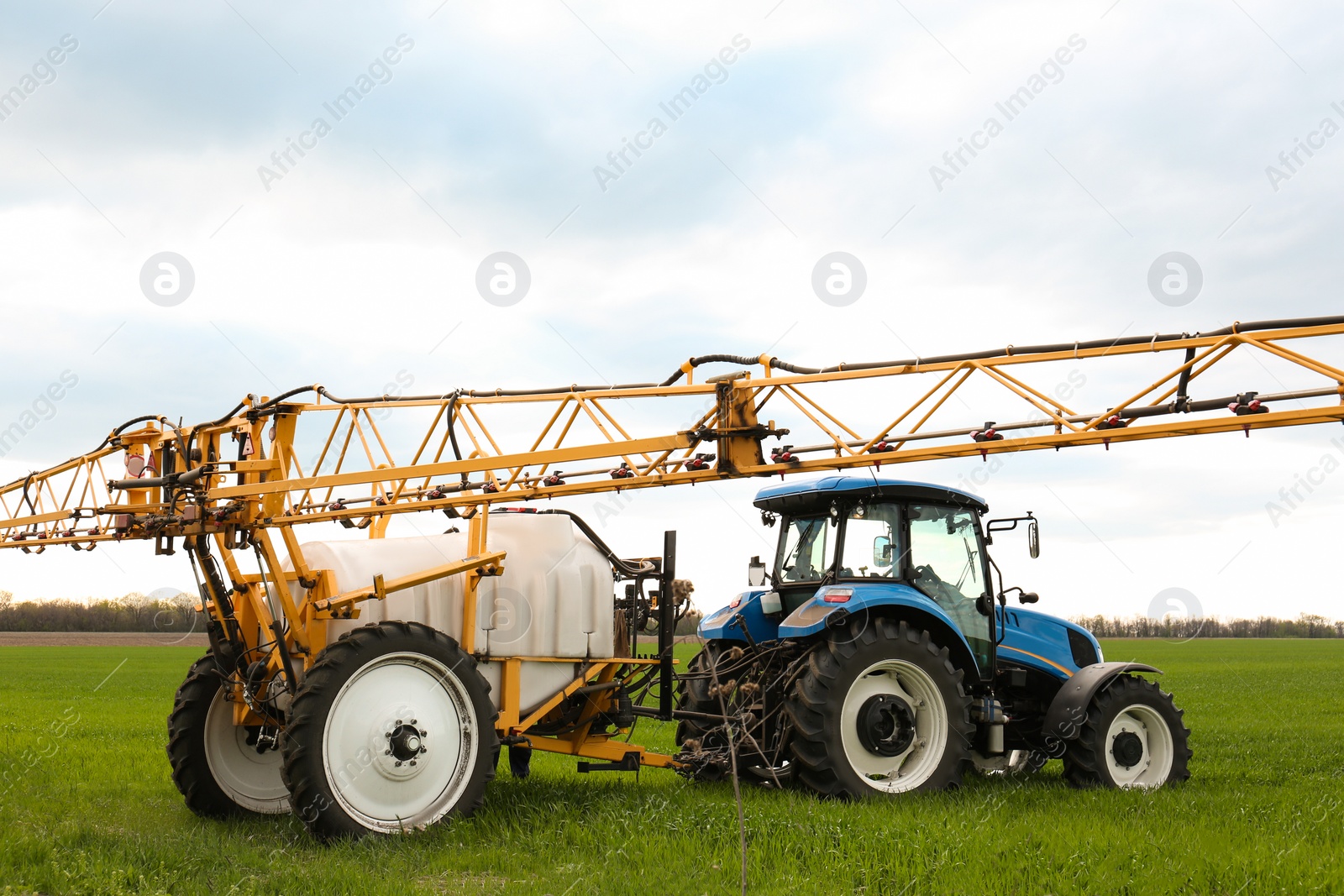 Photo of Tractor spraying pesticide in field on sunny day. Agricultural industry