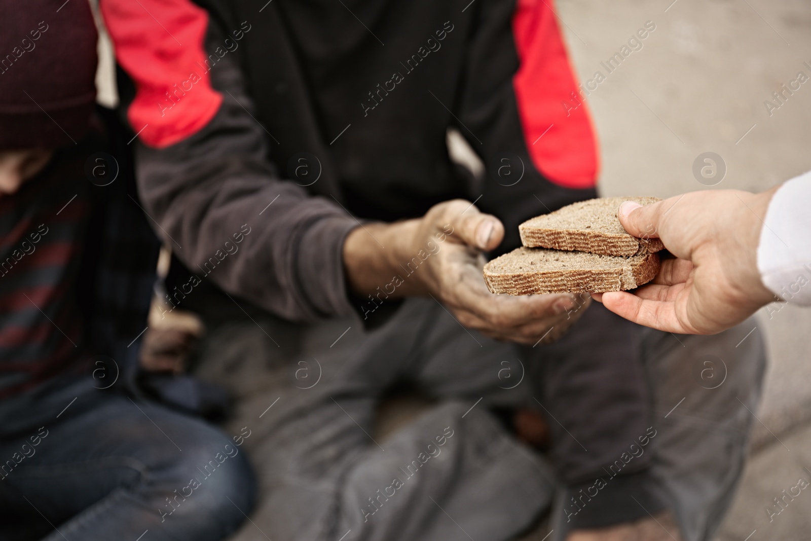 Photo of Woman giving poor homeless people pieces of bread outdoors, closeup