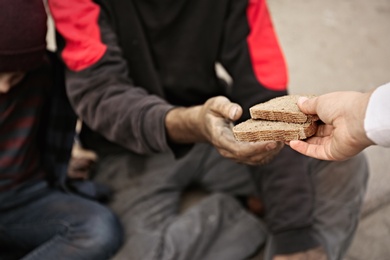 Woman giving poor homeless people pieces of bread outdoors, closeup