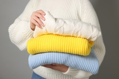 Woman with stack of knitted sweaters on grey background, closeup