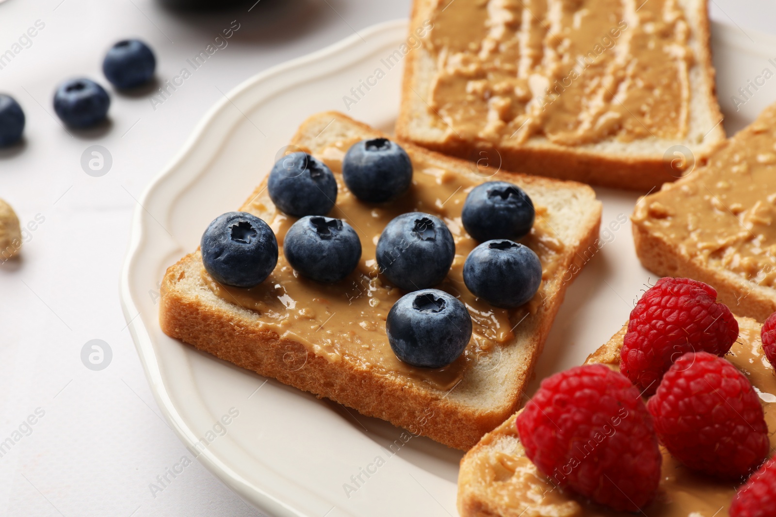 Photo of Delicious toasts with peanut butter, raspberries and blueberries on white table, closeup