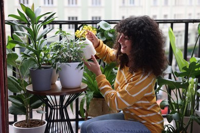 Beautiful young woman watering green houseplants on balcony