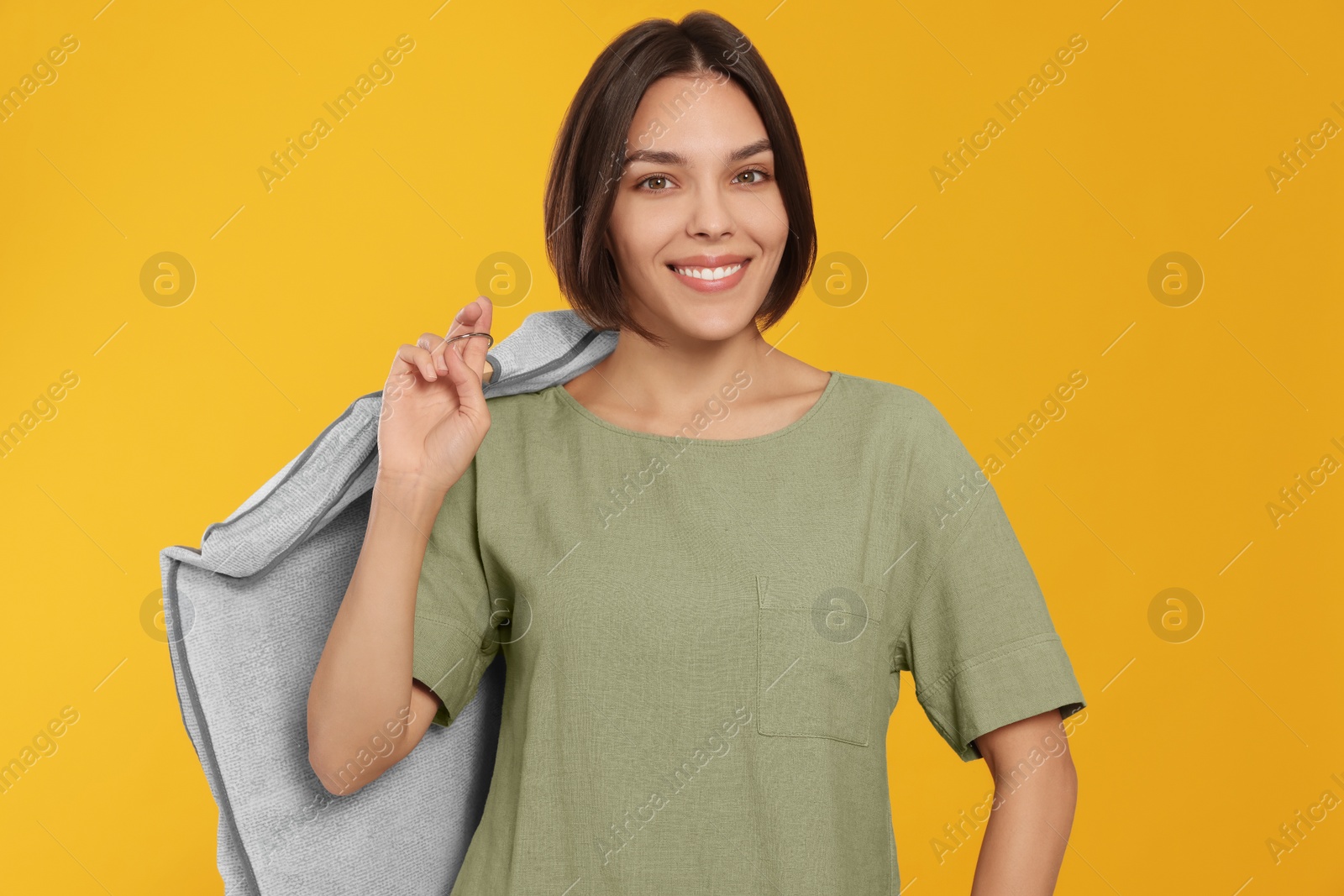 Photo of Woman holding garment cover with clothes on yellow background. Dry-cleaning service