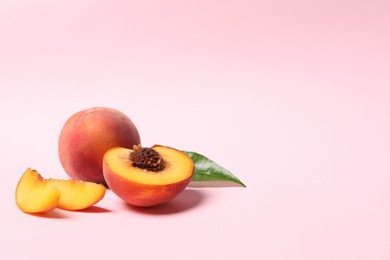 Photo of Delicious juicy peaches and leaf on pink background, space for text