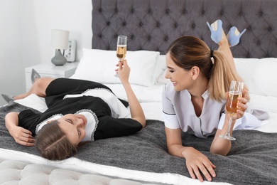 Photo of Young chambermaids lying on bed with glasses of champagne in hotel room