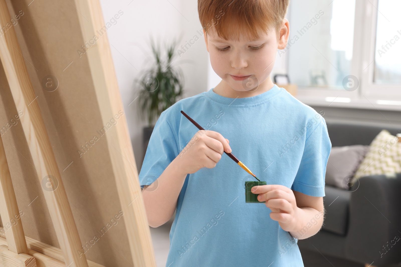 Photo of Little boy painting in studio. Using easel to hold canvas