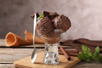 Photo of Tasty chocolate ice cream with mint in glass dessert bowl served on wooden table