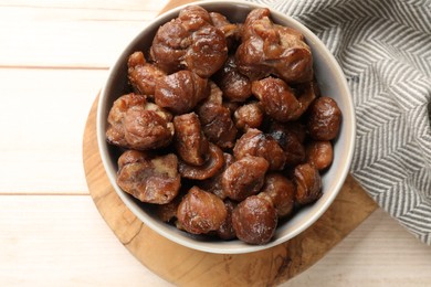 Roasted edible sweet chestnuts in bowl on light wooden table, top view