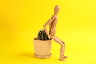 Wooden human figure and cactus on yellow background. Hemorrhoid problems