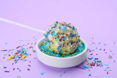 Photo of Delicious confectionery. Sweet cake pop and sprinkles on light violet background, closeup