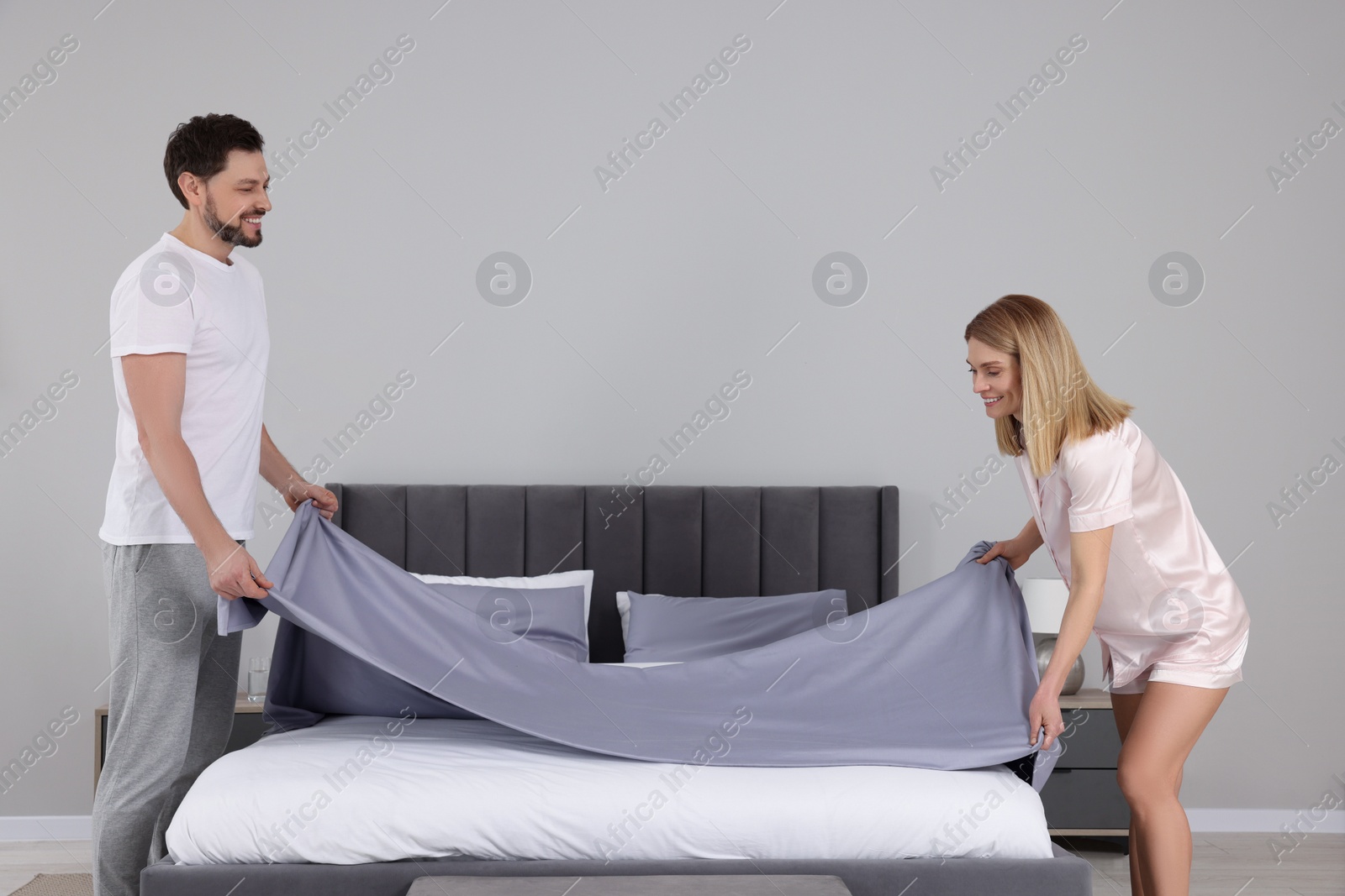 Photo of Couple changing bed linens in room. Domestic chores