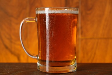 Photo of Mug with fresh beer on wooden table against color background, closeup