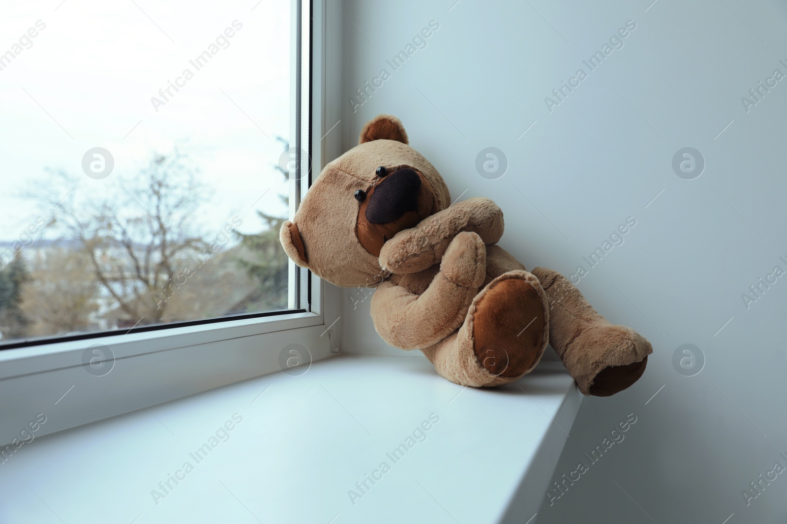 Photo of Cute lonely teddy bear on windowsill indoors