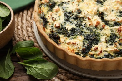 Photo of Delicious homemade quiche and spinach leaves on table, closeup