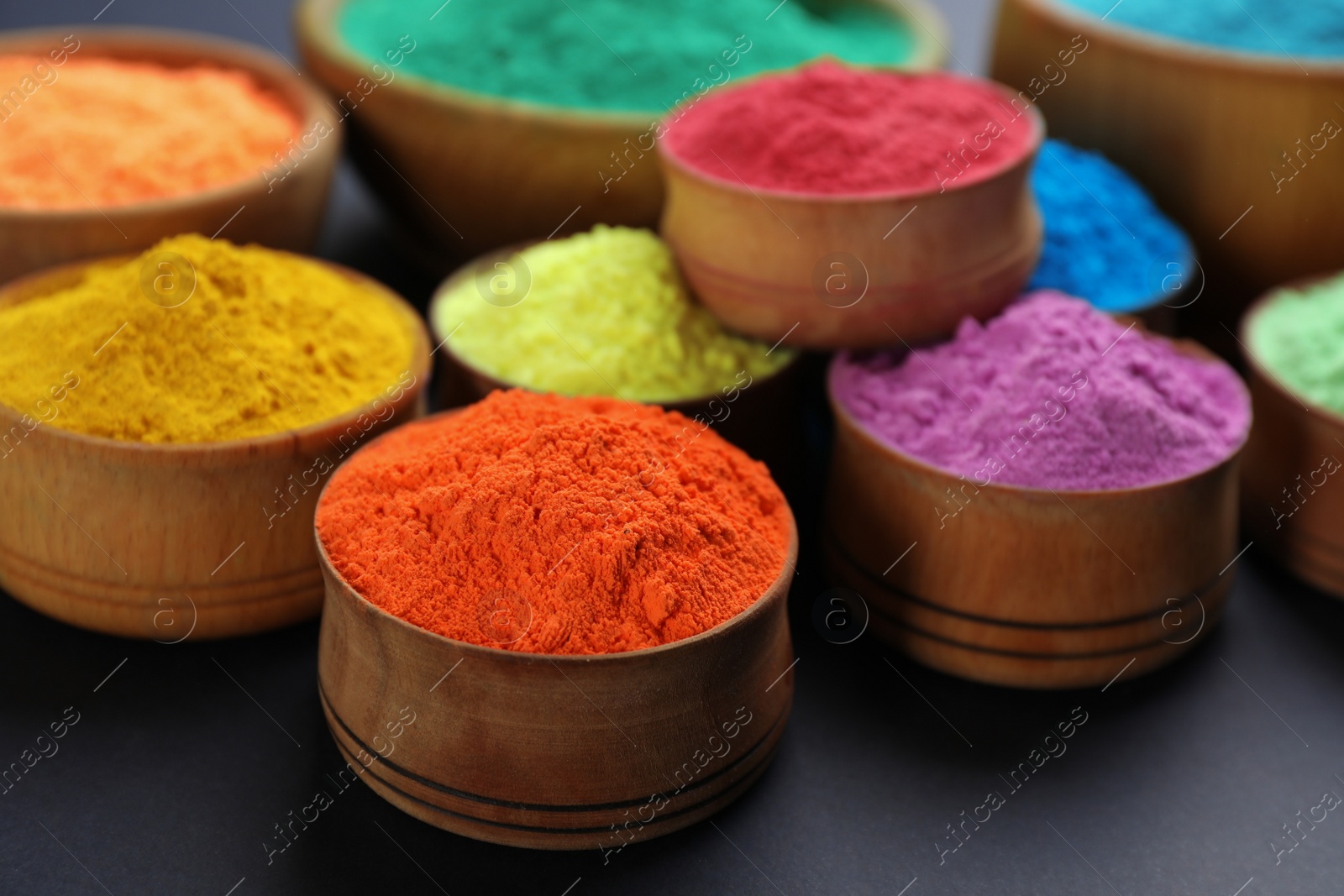 Photo of Colorful powders in wooden bowls on black background. Holi festival celebration