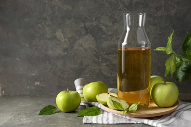 Photo of Delicious cider, ripe apples and green leaves on gray table, space for text