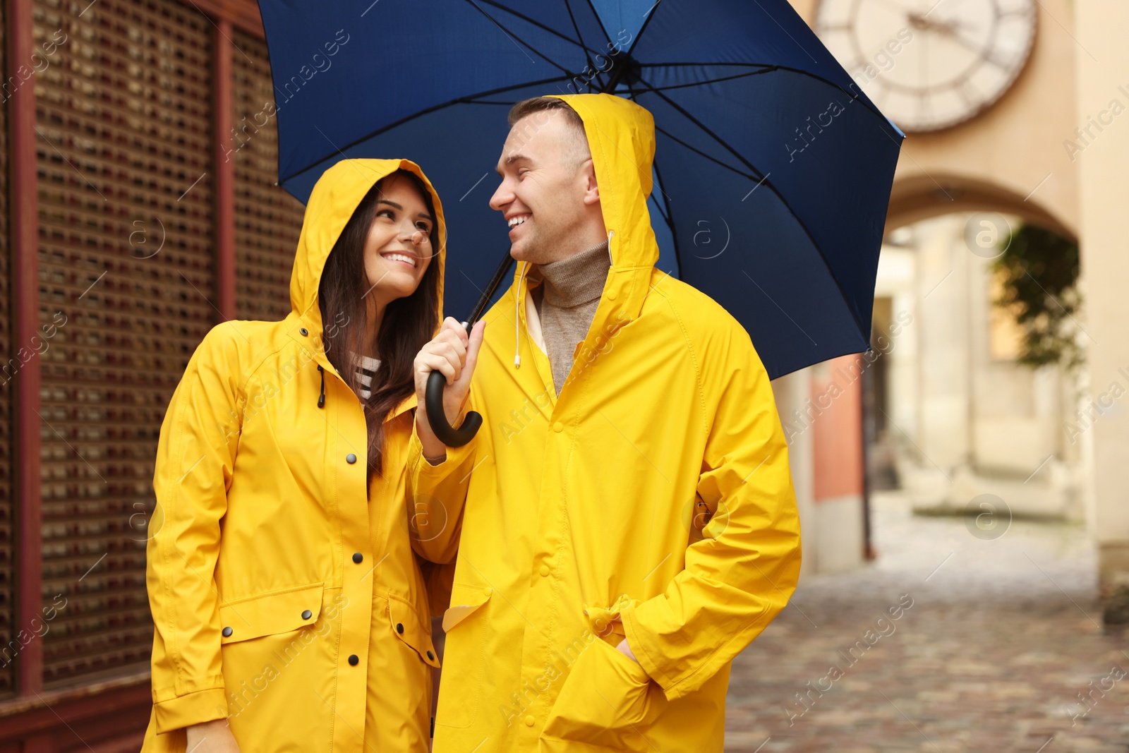 Photo of Lovely young couple with umbrella walking under rain on city street