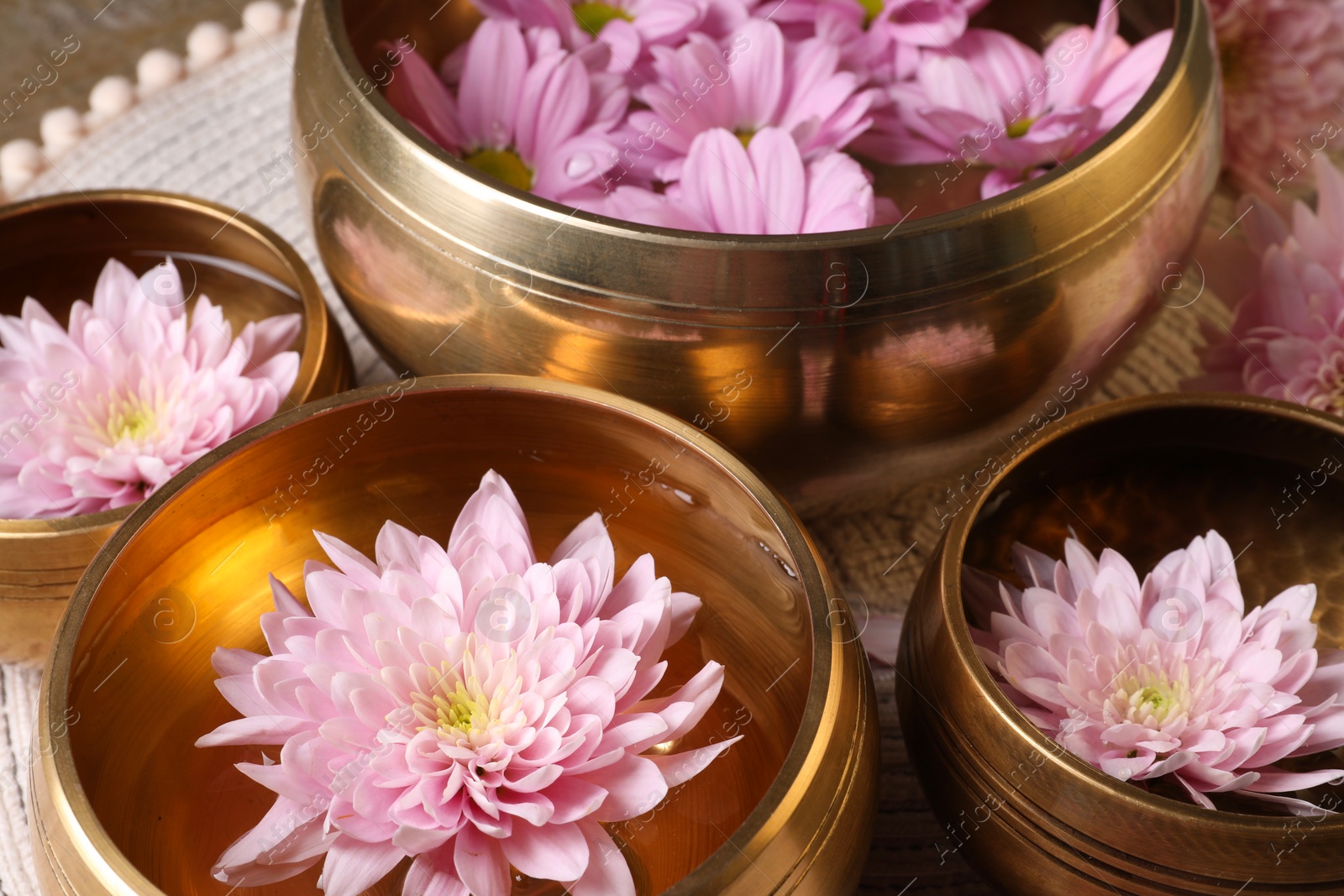 Photo of Tibetan singing bowls with water and beautiful flowers on table, closeup