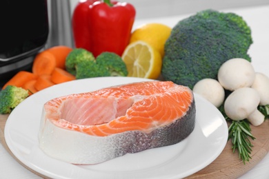 Raw salmon steak and vegetables near multi cooker on table, closeup