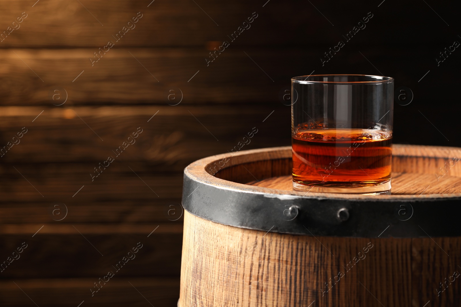 Photo of Glass of tasty whiskey on wooden barrel, space for text