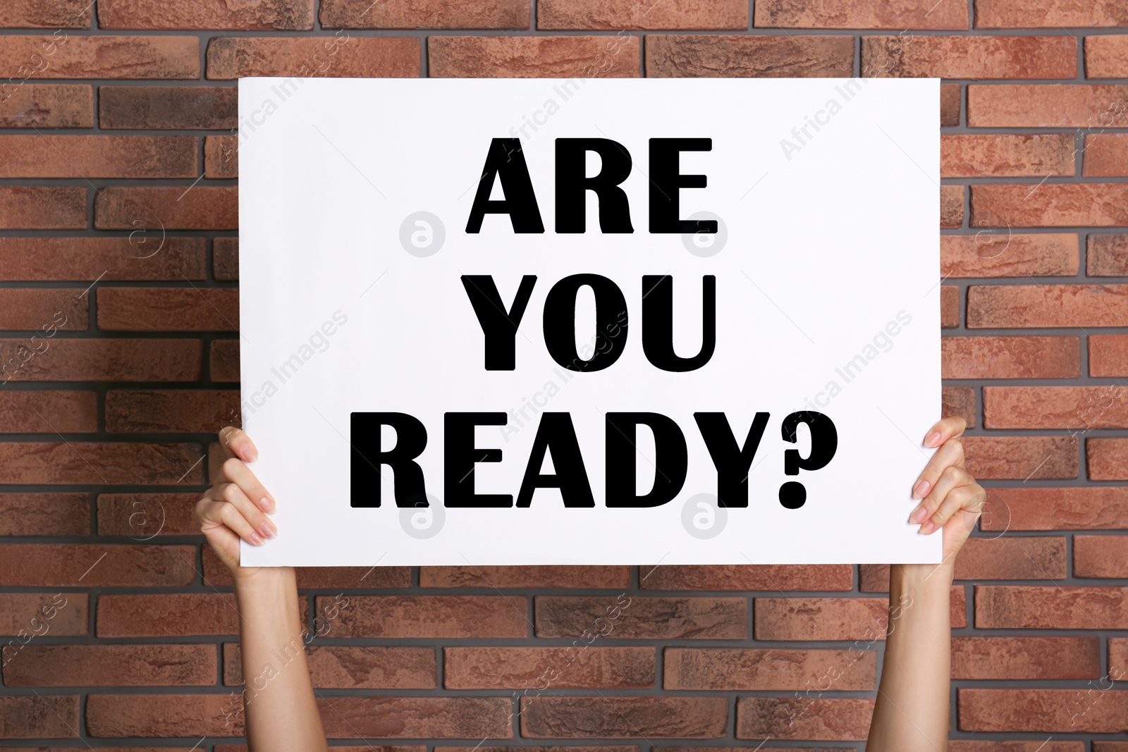 Image of Woman holding poster with text Are You Ready? near red brick wall, closeup