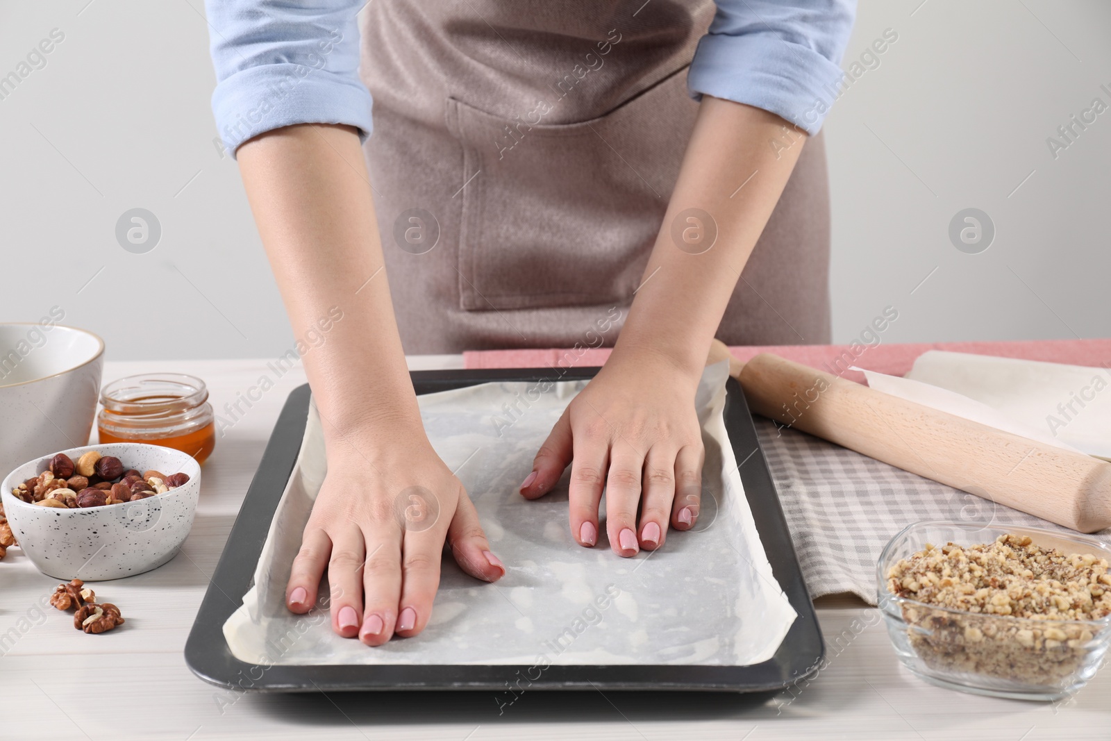 Photo of Woman making delicious baklava at white wooden table, closeup