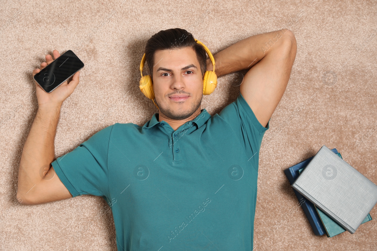 Photo of Man with smartphone listening to audiobook on floor, top view