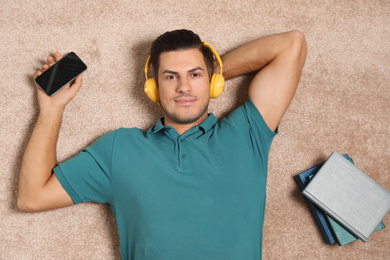 Photo of Man with smartphone listening to audiobook on floor, top view