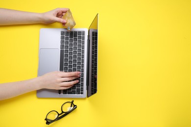 Online payment. Woman with laptop, credit card and glasses on yellow background, top view. Space for text