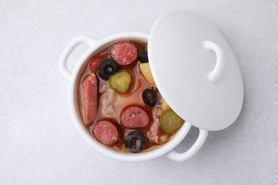 Photo of Meat solyanka soup with thin dry smoked sausages in pot on light table, top view