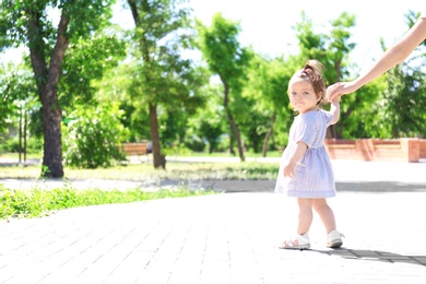 Adorable baby girl holding mother's hand while learning to walk outdoors