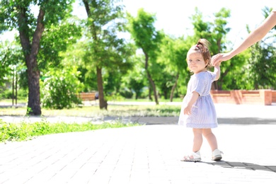 Photo of Adorable baby girl holding mother's hand while learning to walk outdoors