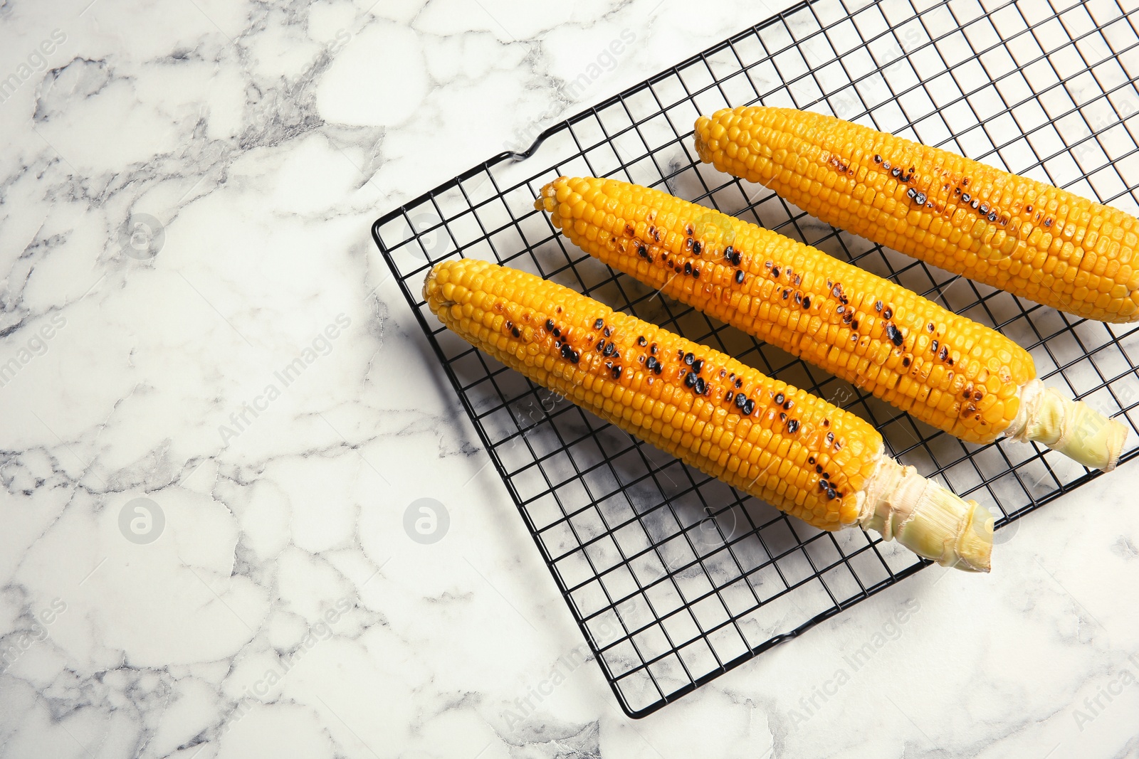 Photo of Cooling rack with grilled corn cobs on marble background, top view. Space for text