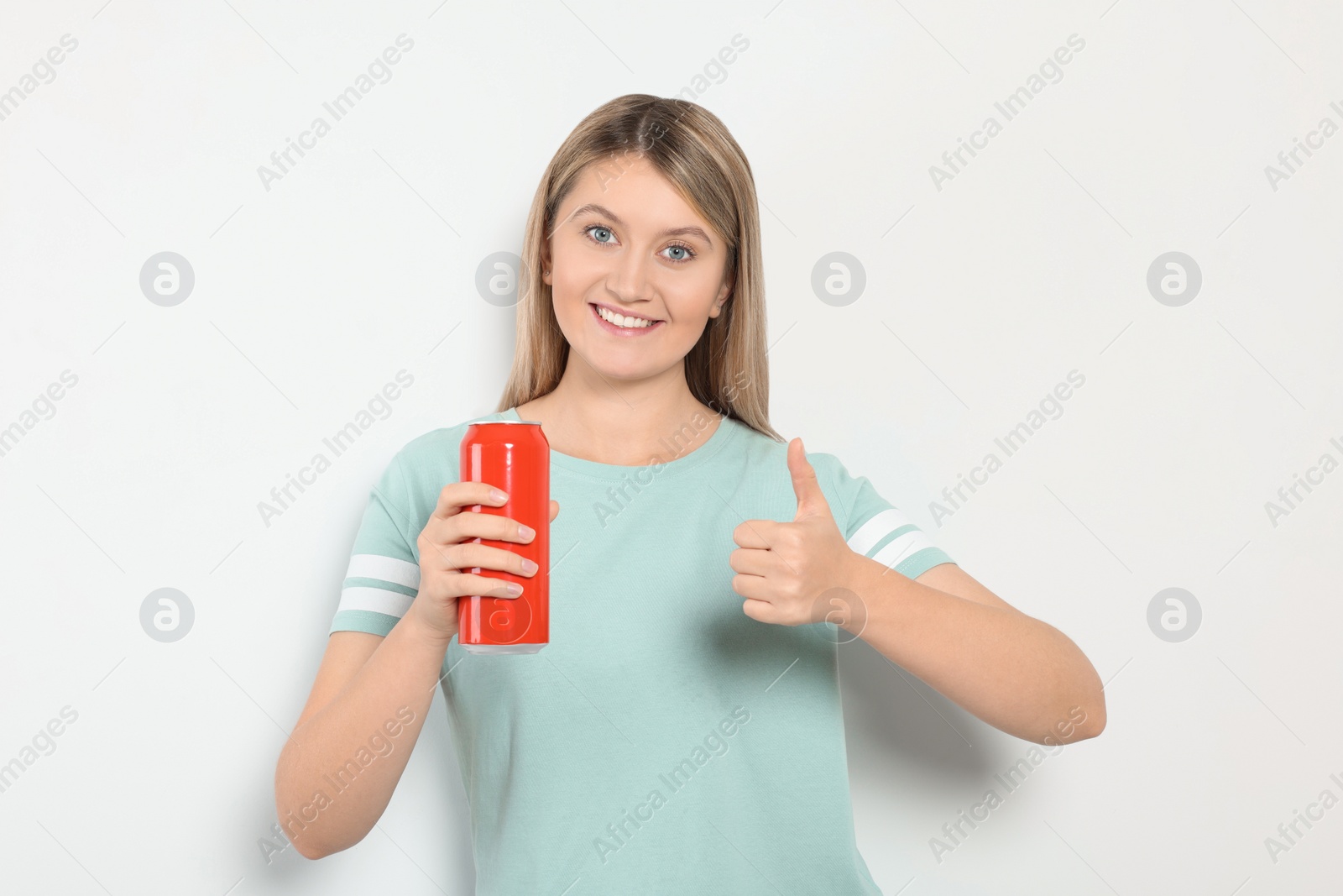 Photo of Beautiful happy woman holding red beverage can and showing thumbs up on light background