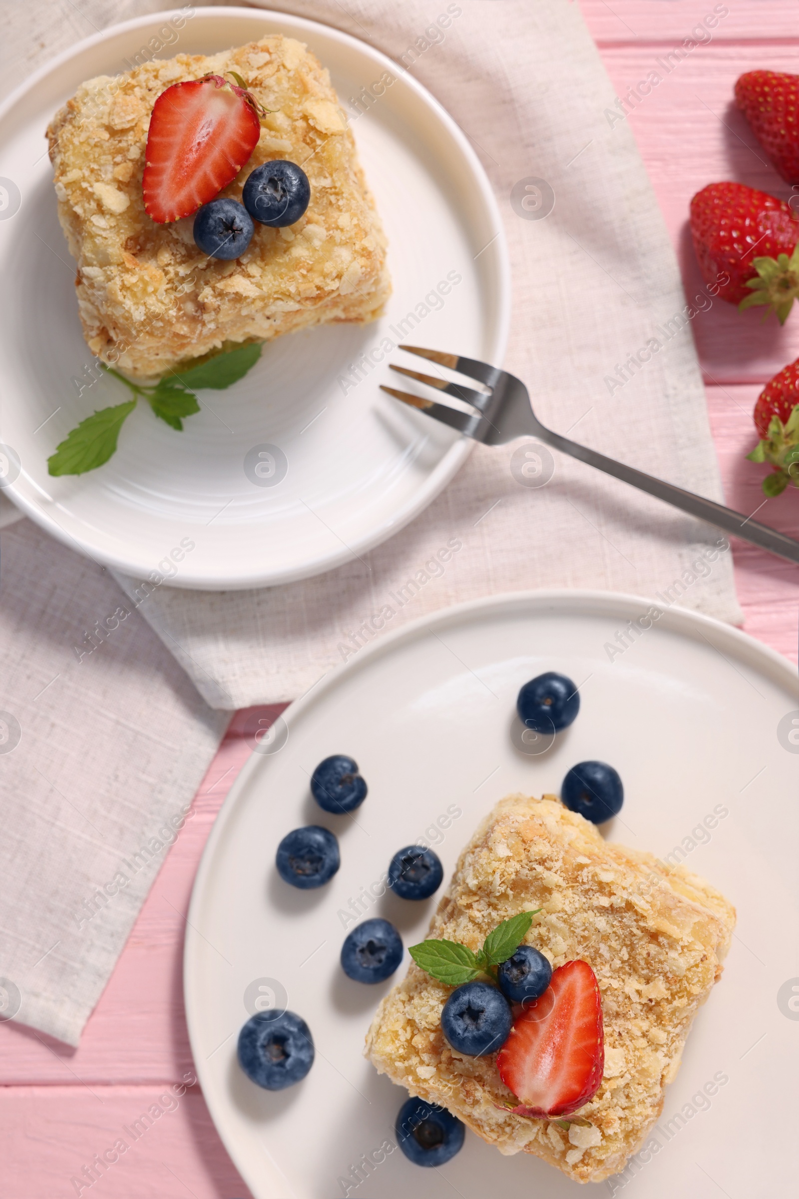 Photo of Pieces of delicious Napoleon cake with fresh berries served on pink wooden table, flat lay