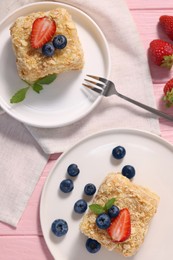 Pieces of delicious Napoleon cake with fresh berries served on pink wooden table, flat lay