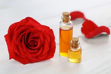 Bottles of essential oil and red rose flower on white wooden table