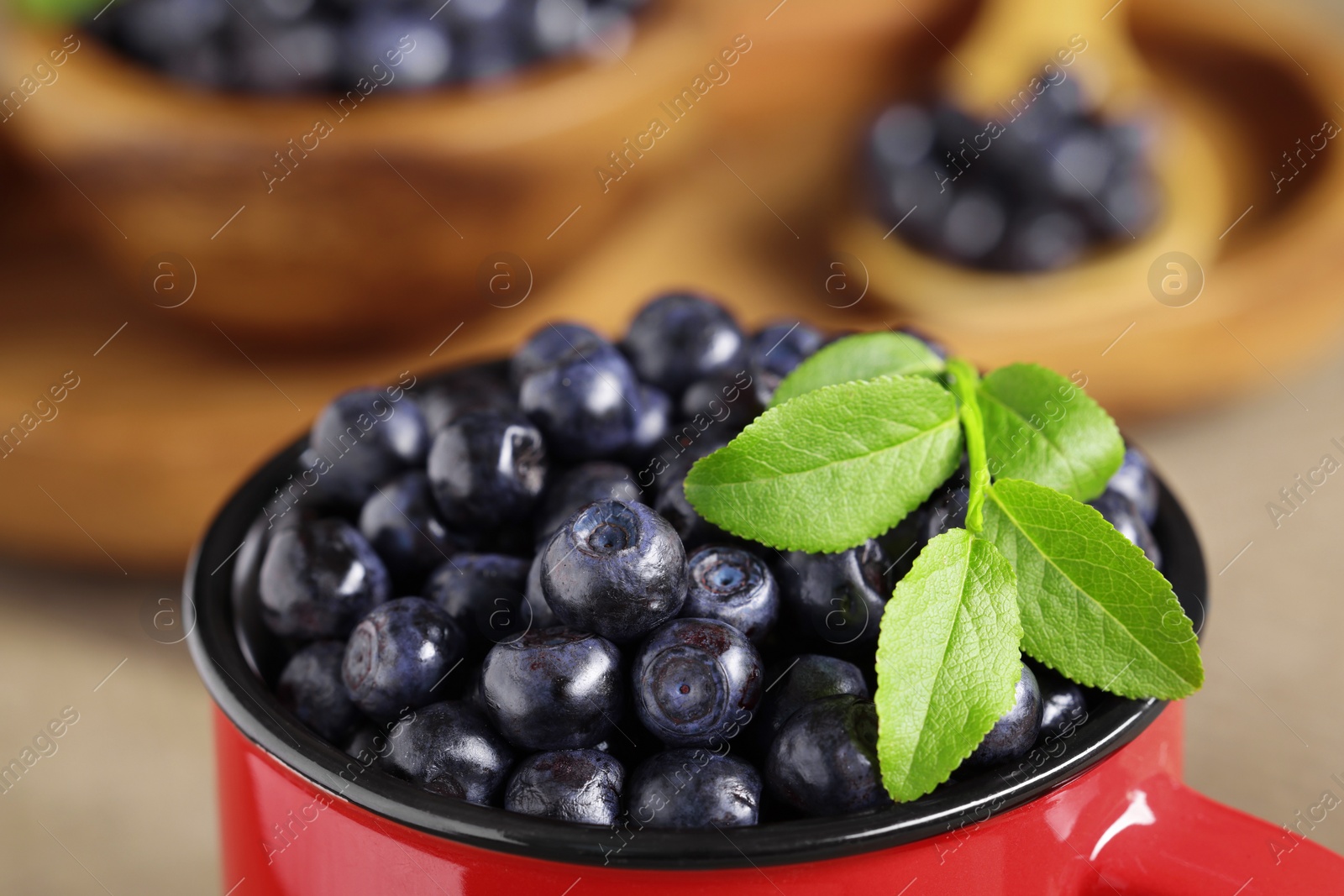 Photo of Tasty fresh bilberries with green leaves in red mug, closeup