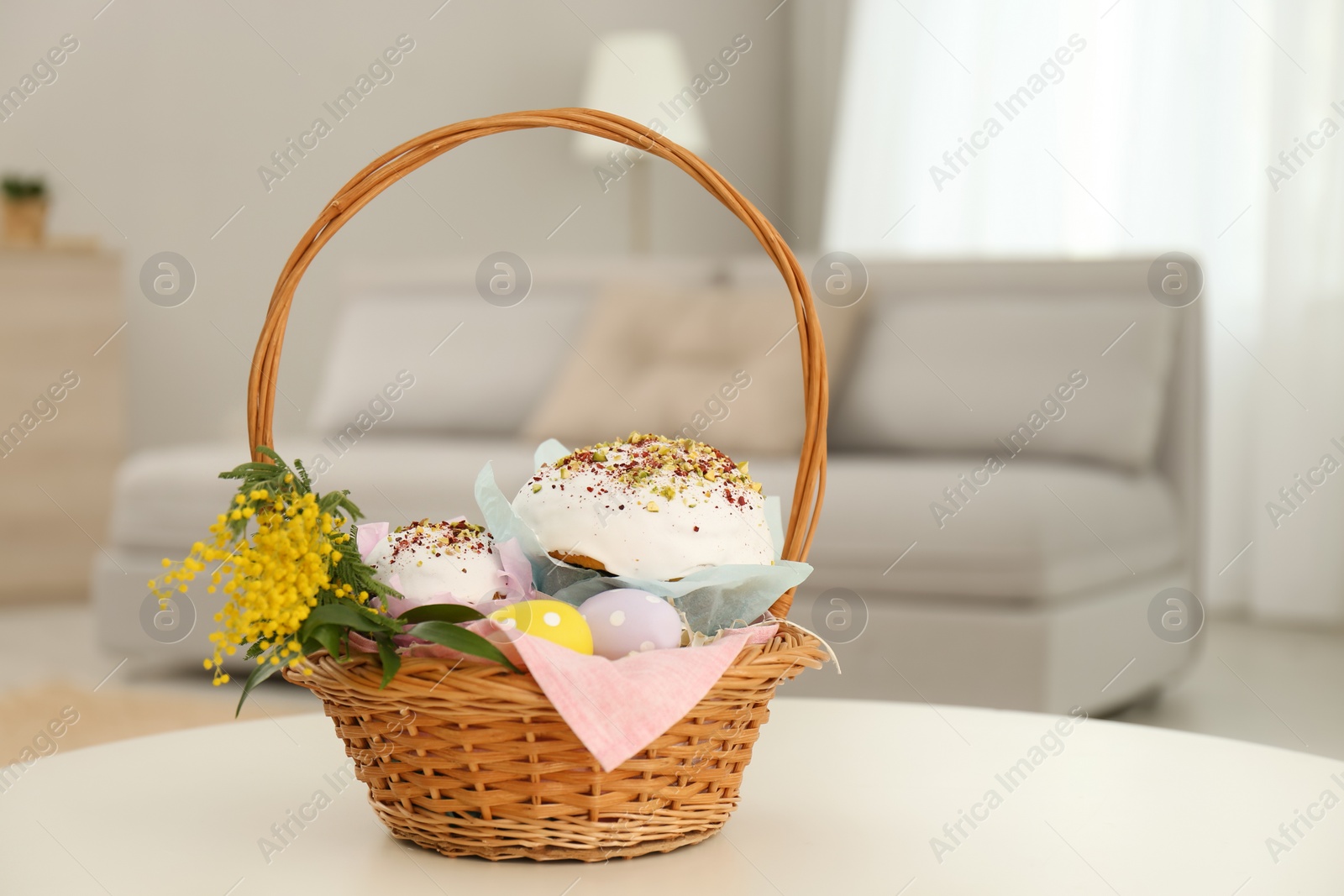 Photo of Basket with delicious Easter cakes, dyed eggs and flowers on white table indoors. Space for text