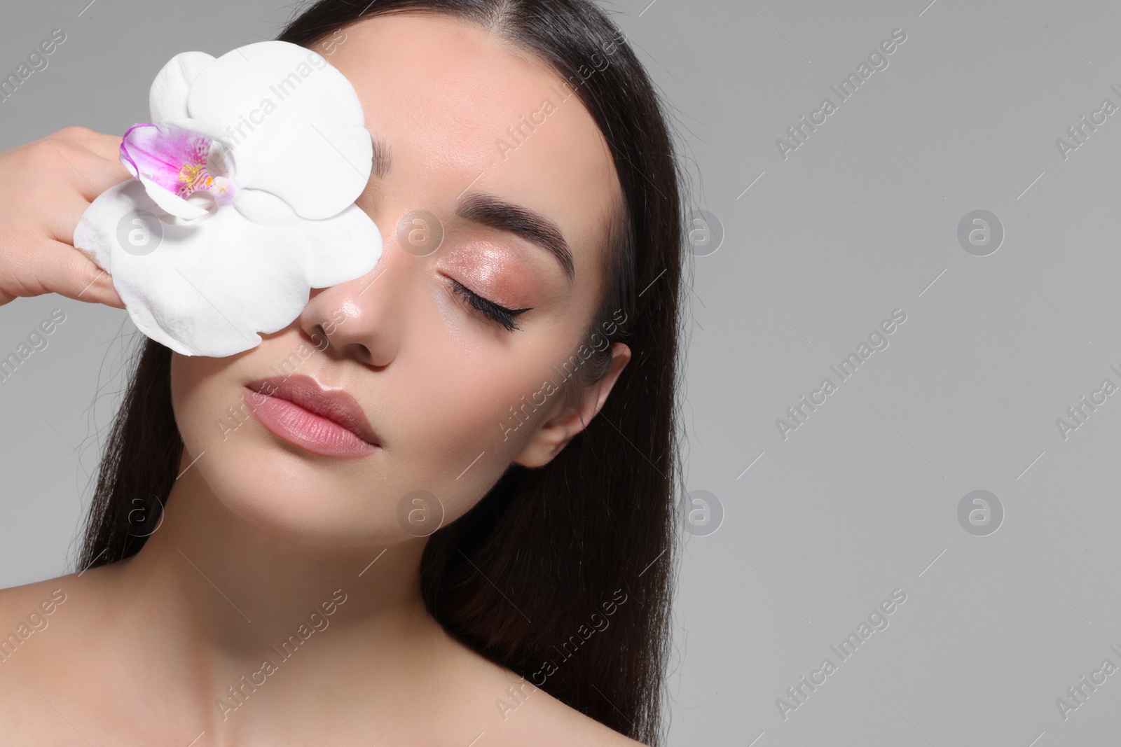 Photo of Beautiful young woman covering eye with orchid flower on grey background. Space for text