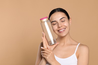 Photo of Young woman with bottle of micellar water on beige background, space for text