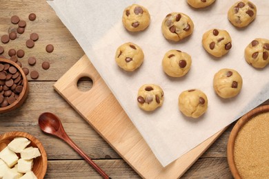 Photo of Unbaked chocolate chip cookies and ingredients on wooden table, flat lay