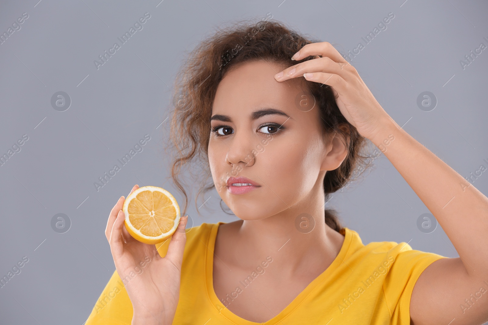 Photo of Beautiful young woman with acne problem holding lemon on grey background. Skin allergy