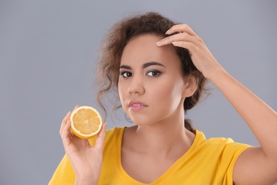 Photo of Beautiful young woman with acne problem holding lemon on grey background. Skin allergy