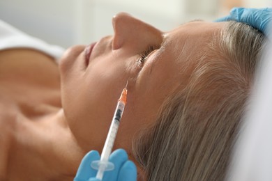 Doctor giving facial injection to senior woman in clinic, closeup. Cosmetic surgery