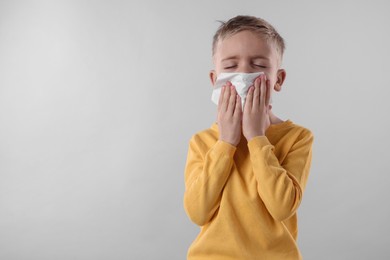 Photo of Sick boy with tissue coughing on gray background, space for text. Cold symptoms